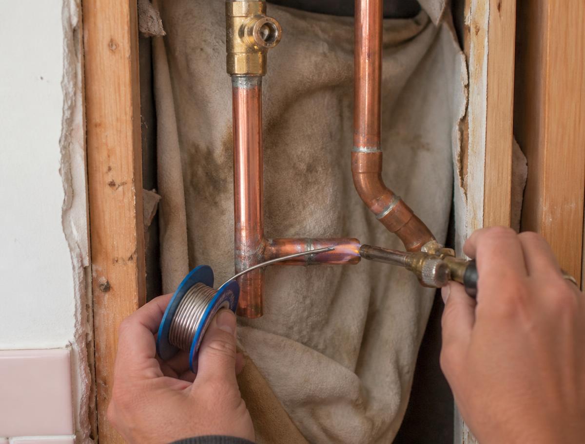 Close up of copper pipe being soldered inside a wall cavity during a bathroom repair